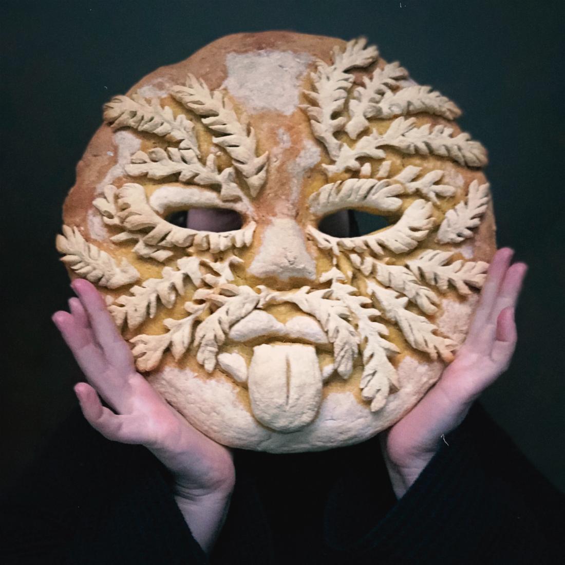 Polina's hands holding a bread mask with leaves on it.