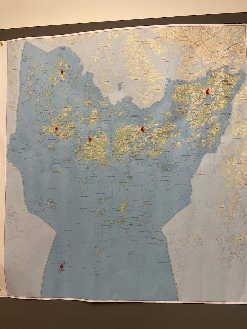 A wall-mounted map with several red pins marking specific locations across various islands and coastal areas.