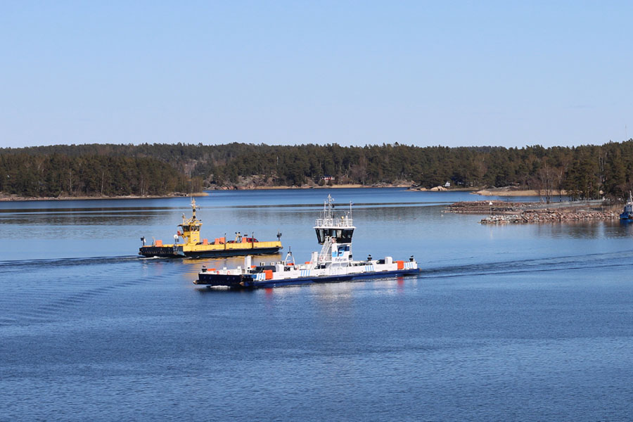 Two ferries cross a calm body of water near a wooded shore under a clear blue sky.